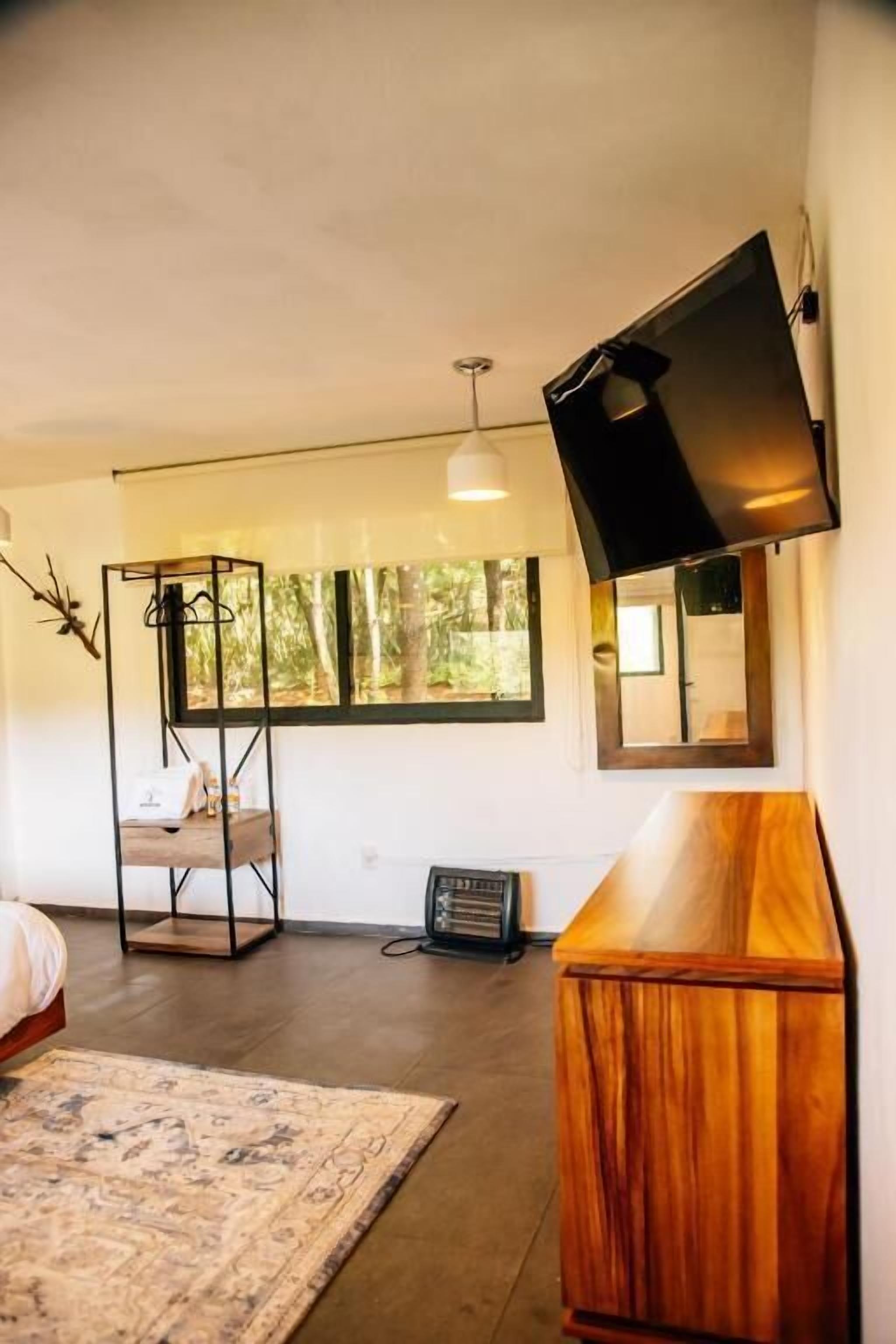 Een moderne slaapkamer met een bed, een houten kast, een aan de muur bevestigde televisie en een raam met uitzicht op bomen.