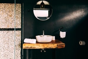 Een badkamer met een ronde spiegel, een witte wastafel, een houten aanrechtblad en een handdoekhouder.