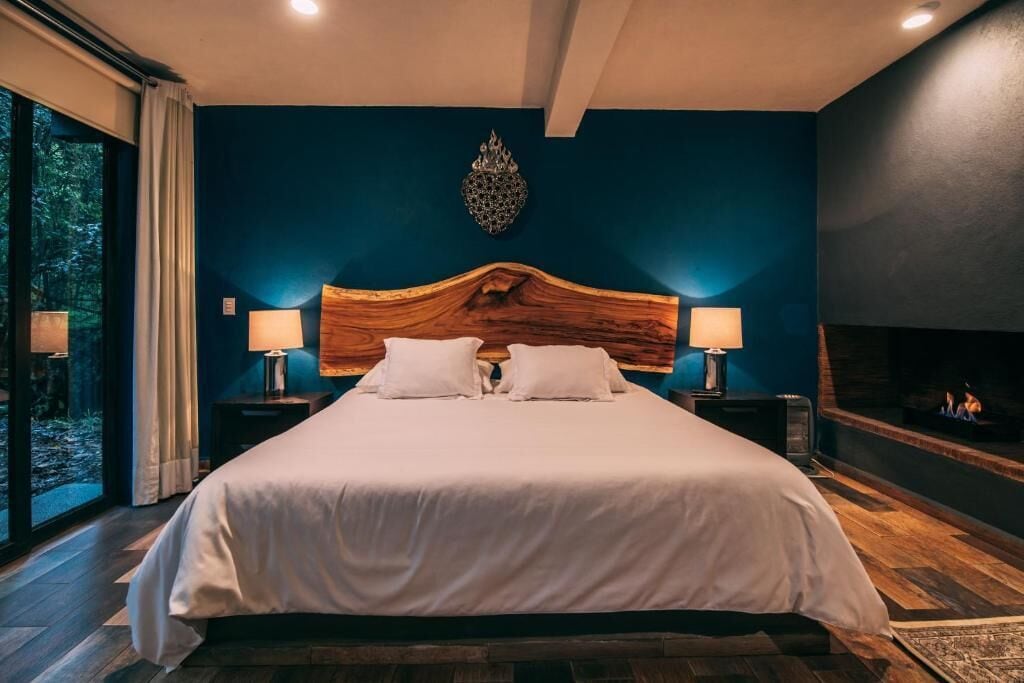 A large bed with a wooden headboard, two bedside lamps, and a fireplace.
