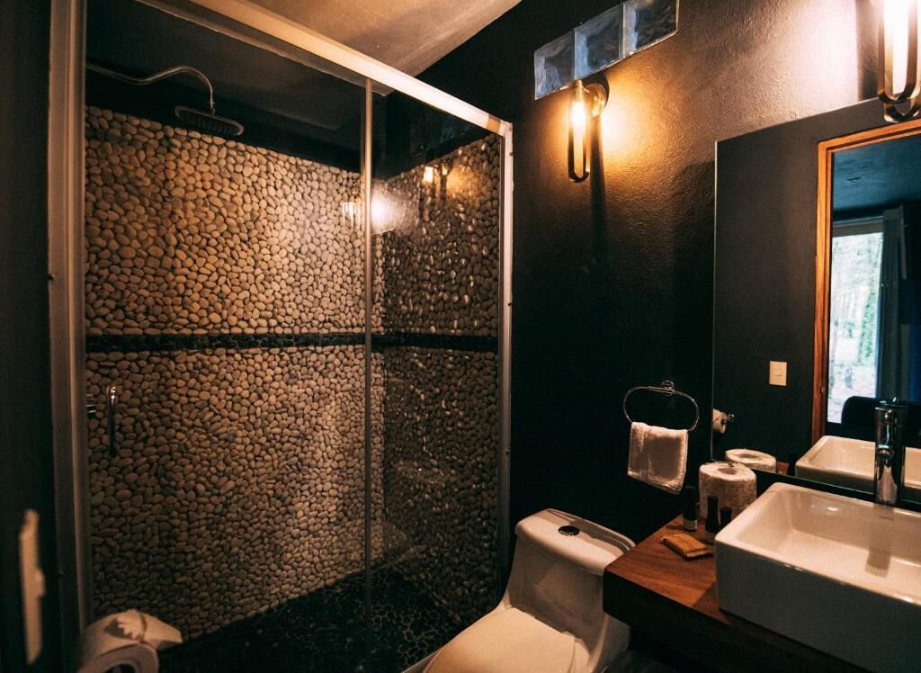 A bathroom with a glass-enclosed shower, a white toilet, a wooden vanity with a sink, and a mirror.