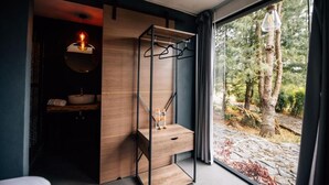 Ein modernes Badezimmer mit einem hölzernen Waschtisch, einer Pendelleuchte und Blick auf einen Wald durch ein großes Fenster.