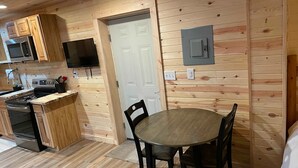 Une cuisine compacte avec un lambris en bois, un coin repas avec une table ronde et des chaises, et un téléviseur fixé au-dessus du comptoir.