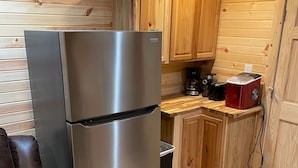 Une cuisine compacte avec des meubles en bois, un réfrigérateur en acier inoxydable, une machine à café rouge et un fauteuil en cuir.