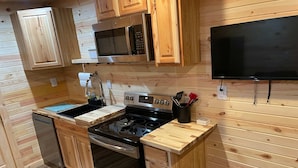 Une cuisine compacte avec des meubles en bois, un four à micro-ondes, une cuisinière et un téléviseur noir fixé au mur.