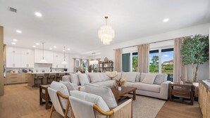 A spacious living area with a large sofa, wooden chairs, a coffee table, and a chandelier. - Ocean Hammock Luxury with Pool, Game Room & Beach Access (Palm Coast)