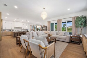 A spacious living area with a large sofa, wooden chairs, a coffee table, and a chandelier. - Ocean Hammock Luxury with Pool, Game Room & Beach Access (Palm Coast)