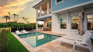 A modern two-story house with a swimming pool, outdoor seating, and a view of palm trees. - Ocean Hammock Luxury with Pool, Game Room & Beach Access (Palm Coast)