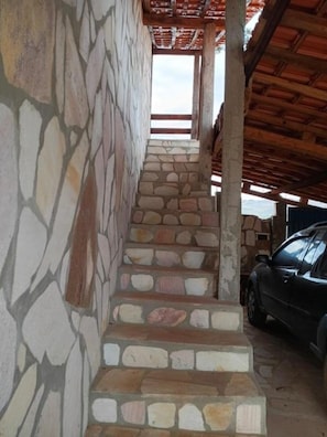 A stone staircase leading to a covered area with a car parked nearby.