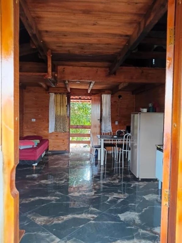 A wooden cabin interior with a bed, a dining table with chairs, a refrigerator, and a kitchen area.