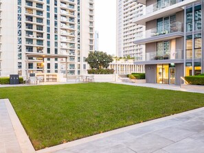A modern residential building with a well-maintained lawn, outdoor seating area, and a glass facade. - SettlerHomes, Breathtaking View With Private Beach (Dubai)