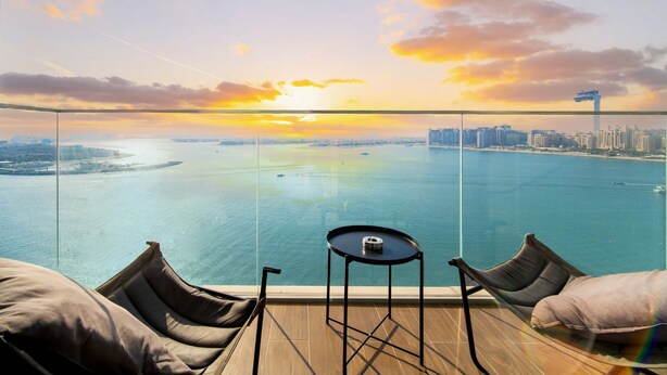 Un balcone con vista su un tramonto sull'acqua, un tavolo e due sedie.