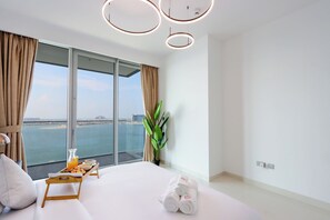 Une chambre d’hôtel moderne avec un grand lit, une petite table avec un plateau de petit-déjeuner, une plante et une vue sur la mer.