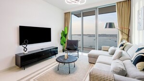 Un soggiorno moderno con una TV a schermo piatto, un mobile TV nero, un tavolino rotondo, un divano grigio e una grande finestra vista mare.