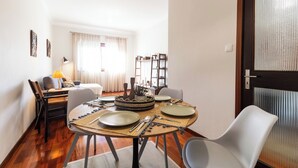 A dining area with a round table set for four, a sofa, and a bookshelf in the background. - Porto Essence Apartment (Porto)