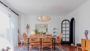 A dining area with a round table, wicker chairs, a patterned rug, and a pendant light.