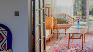 An open doorway leading to a room with a wicker chair, a small table, and a colorful rug.