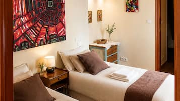 Habitación de hotel con dos camas, aire acondicionado instalado en la pared, mesita de noche con lámpara y obras de arte en las paredes.