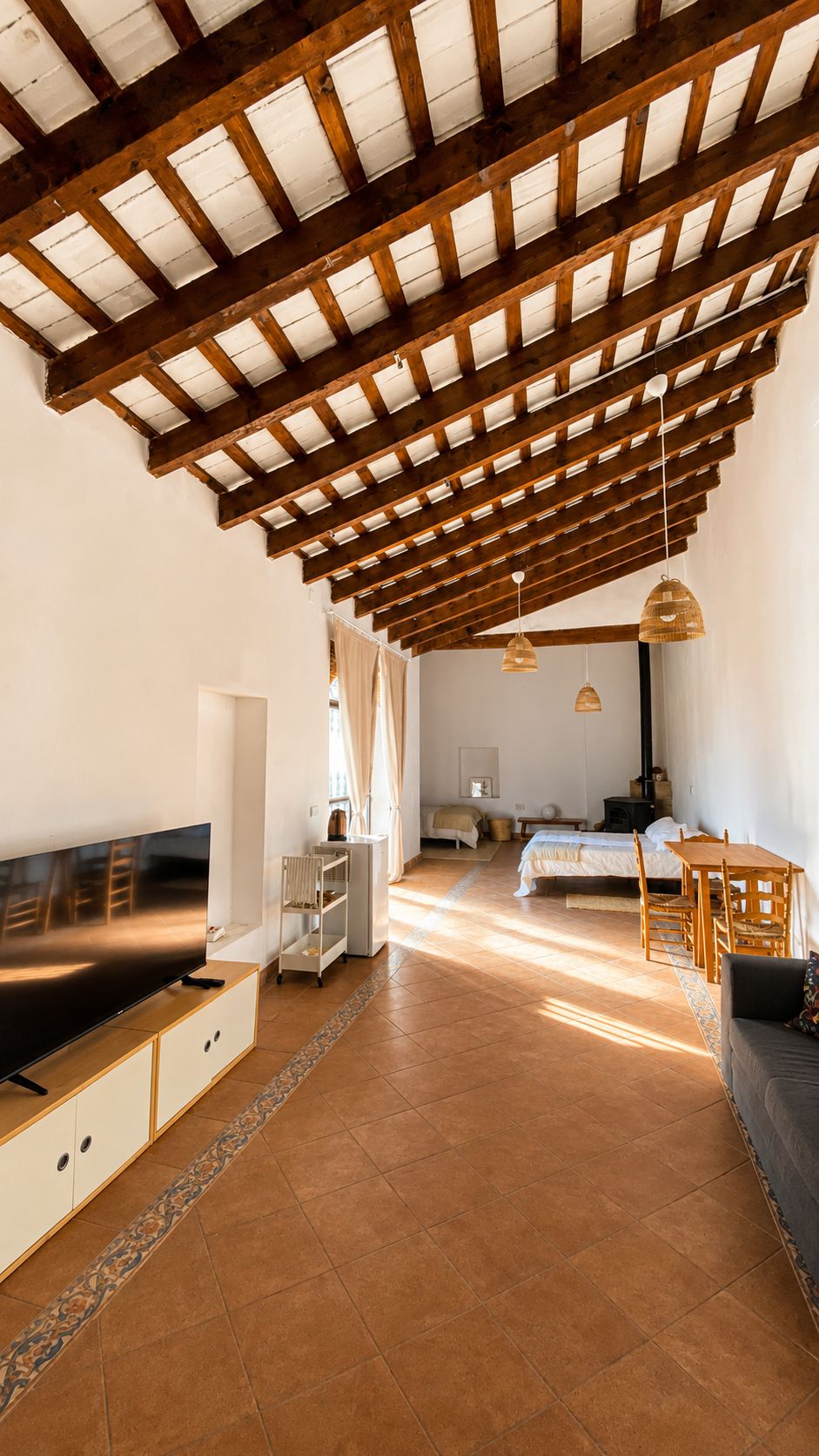 Amplia sala de estar con techo alto, vigas de madera, televisor de pantalla plana, mesa de comedor y sofá.