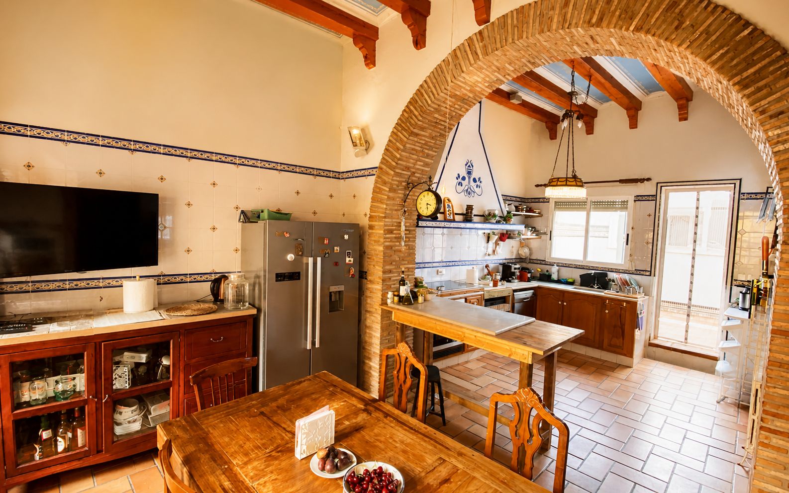 A kitchen with a wooden table, chairs, a refrigerator, and a television.