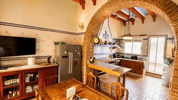 A kitchen with a wooden table, chairs, a refrigerator, and a television.