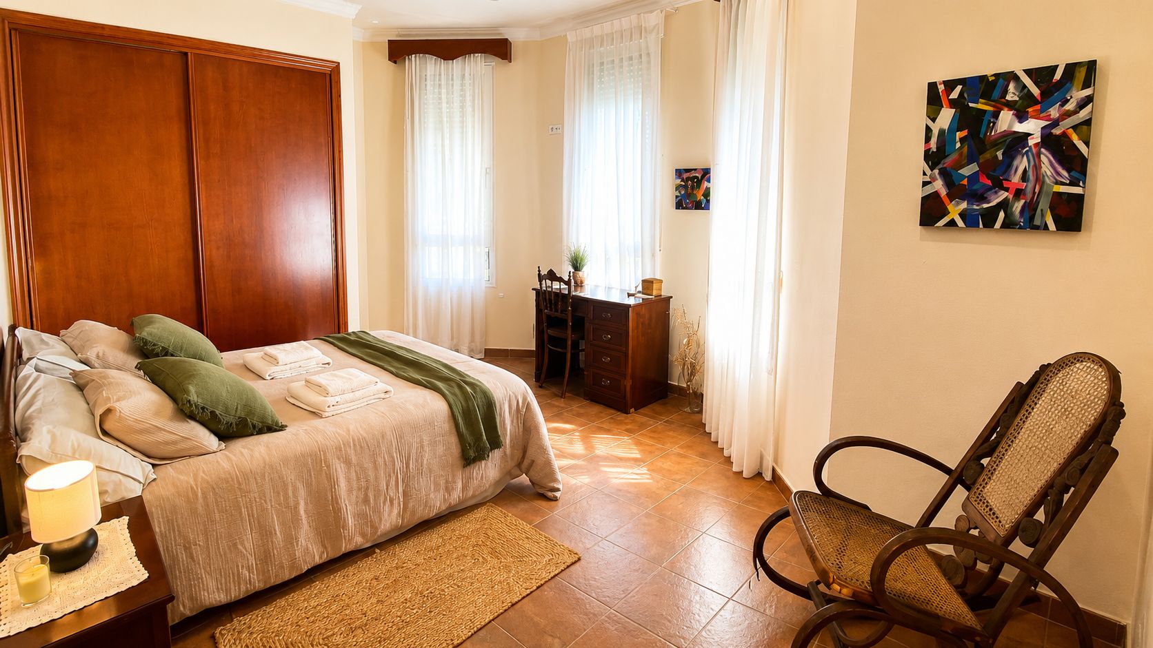 A bedroom with a bed, a chair, a desk, and a painting on the wall.