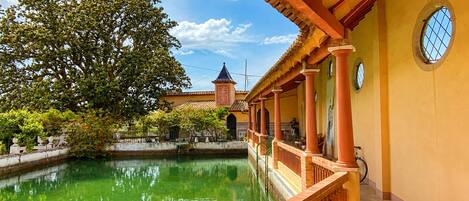 Un patio con piscina, un edificio tradicional con techo de tejas y un árbol.