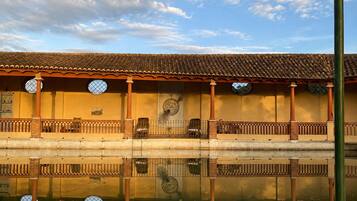 A building with a tiled roof, a balcony with a railing, and a reflection in the water.