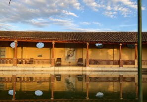 A building with a tiled roof, a balcony with a railing, and a reflection in the water.