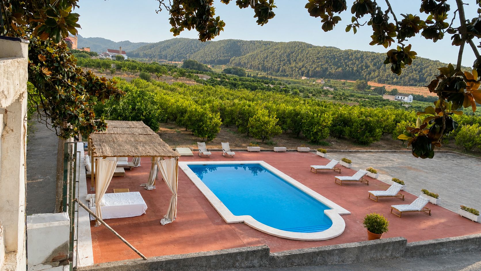 Una piscina con sillones de descanso y una zona de estar cubierta, rodeada de vegetación y colinas.