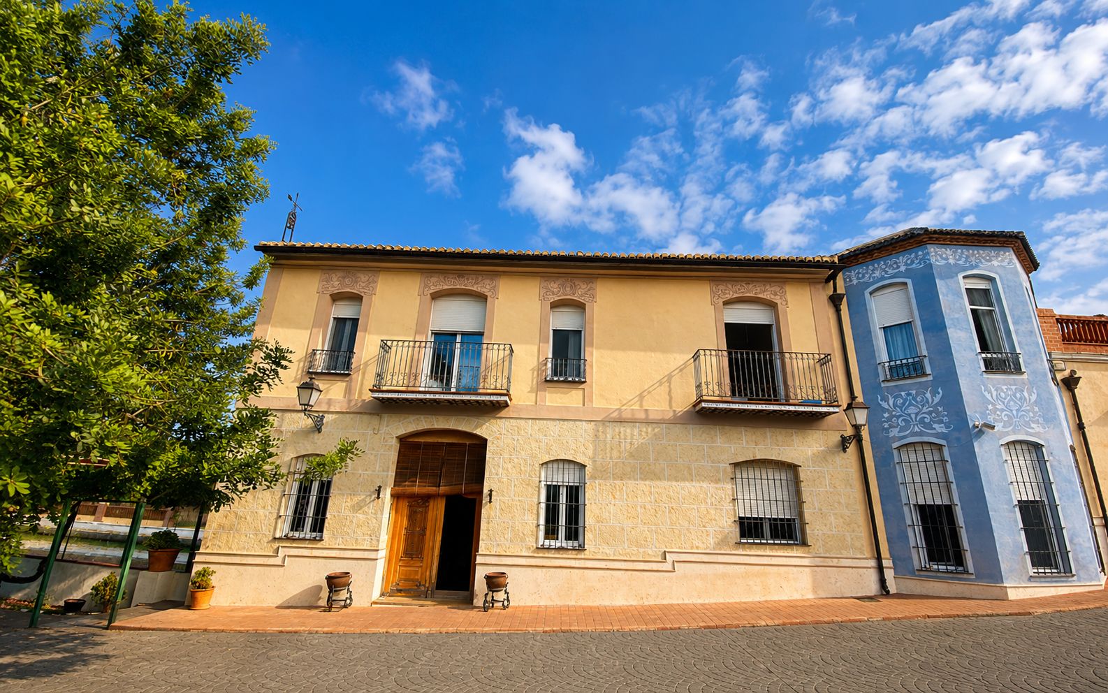A two-story building with a central entrance, balconies, and a corner tower.