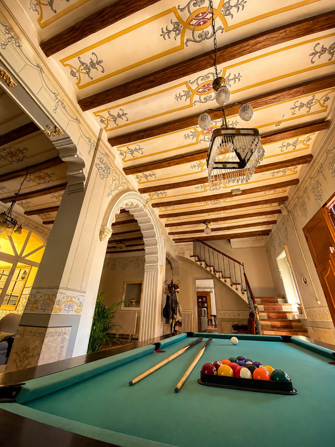 Una sala de billar con mesa de pool, vigas de madera y decoraciones ornamentales en el techo.