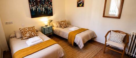 A bedroom with two beds, a nightstand, a chair, and artwork on the wall.
