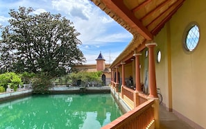 A courtyard with a pool, a large tree, and a building with a tiled roof and a tower.