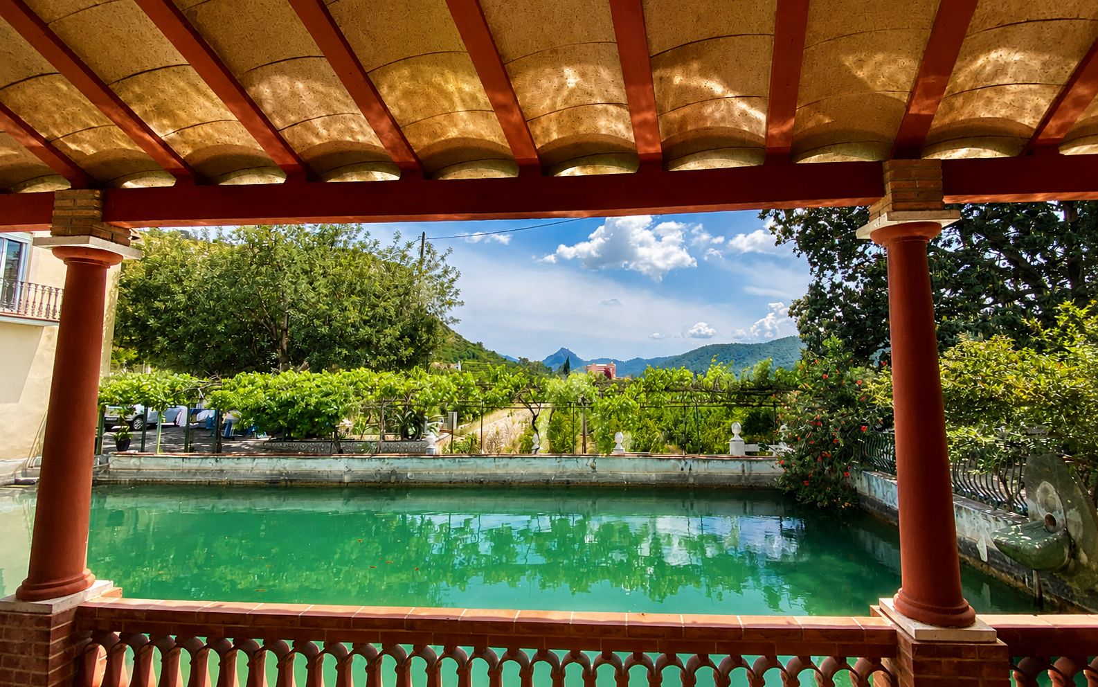 Una piscina con una pérgola encima, rodeada de follaje y un paisaje montañoso.