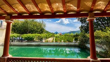 Una piscina con una pérgola encima, rodeada de follaje y un paisaje montañoso.