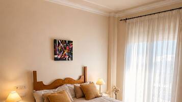 Una cama bien hecha con cabecera, lámparas de noche y un cuadro en la pared.