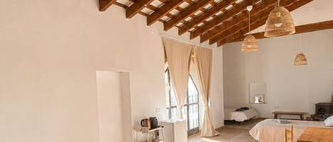 A spacious bedroom with a large bed, a wooden ceiling, and a view of the kitchen.