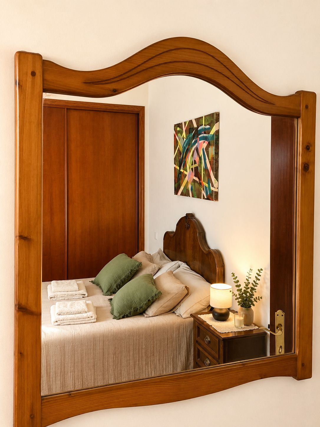 Una cama con cabecera de madera, una mesita de noche con lámpara y un espejo.