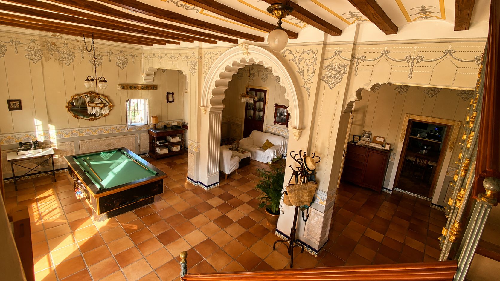 Una mesa de billar en una habitación con piso de baldosas, techo de madera y un arco decorativo.