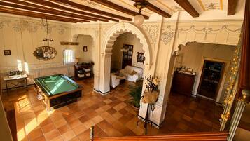 Una mesa de billar en una habitación con piso de baldosas, techo de madera y un arco decorativo.