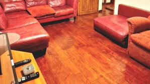 Un salón con un sofá de cuero rojo, un reposapiés a juego y una mesa de centro de madera con mandos a distancia.