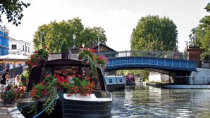 Un barco canalero amarrado en la orilla de un río, con un puente azul al fondo.