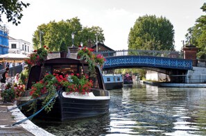 Ein Kanalboot liegt an einer Flussuferanlage, im Hintergrund eine blaue Brücke.