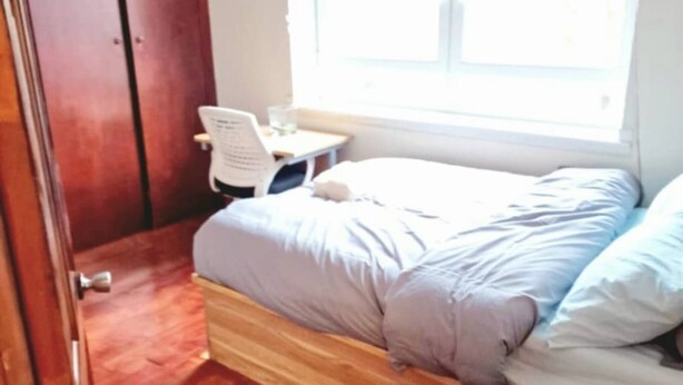 Un dormitorio con cama, suelo de madera, armario y ventana con persianas.