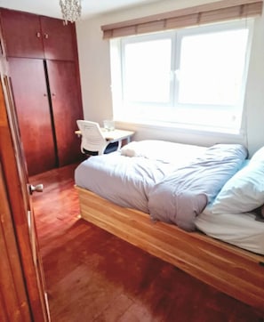 A bedroom with a bed, wooden floor, wardrobe, and a window with blinds. - Whole Flat in Little Venice (London)