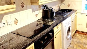 Una cocina con armarios color beige, encimera negra, extractor de acero inoxidable, lavadora y salpicadero de azulejos.