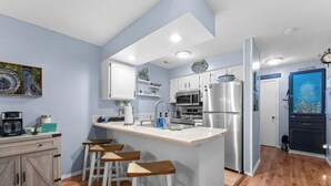A modern kitchen with a central island, bar stools, a refrigerator, and a microwave. - Pretty Peacock: 2BR/2BA near SDC & Lake Access! (Branson West)