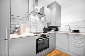 A modern kitchen with grey cabinets, a built-in oven, a microwave, and a stainless steel range hood. - Uebert Heights| 2Bed| Slp6| Closest to Cannock Town (5min walk)| Free Parking (Cannock)