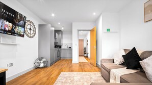 A modern living room with a flat-screen TV, a clock, a fan, and a sofa. - Uebert Heights| 2Bed| Slp6| Closest to Cannock Town (5min walk)| Free Parking (Cannock)