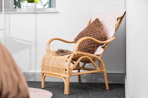 A wicker chair with a fur throw and a pillow, positioned against a white wall with a window above. - Uebert Heights| 2Bed| Slp6| Closest to Cannock Town (5min walk)| Free Parking (Cannock)